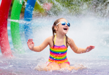 girl in rainbow swimsuit sits in rainbow splash pad